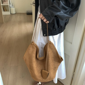 Detailed close-up of brown suede tote bag with slim shoulder straps and matching charm