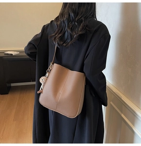 Deep brown pebble leather bucket bag with cute bear charm worn by a model from behind