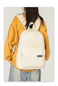 Detail view of the cream canvas backpack with a front zipper pocket and logo label