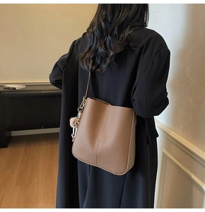 Detail of caramel lychee grain leather bucket bag with pink plush keychain charm
