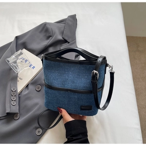 Detail of blue denim bucket bag featuring black leather trim and adjustable shoulder strap