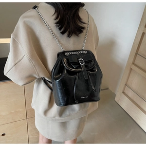 Detail of black patent leather mini backpack with bow, silver chain, and logo print