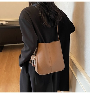 Close-up of brown litchi pattern bucket bag with pom-pom charm on female model