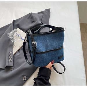Detailed macro view of denim bucket bag with black leather handles and adjustable strap