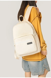 Close-up of a white canvas backpack with front zipper pocket and side water bottle holders