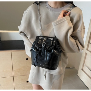 Detail of black glossy mini backpack with bow decoration and silver chain strap