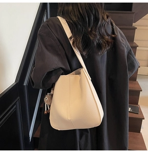 Close-up of beige lychee grain leather tote bag with stylish brown pompom charm