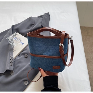 Detail view of denim bucket bag featuring brown leather handles and silver hardware