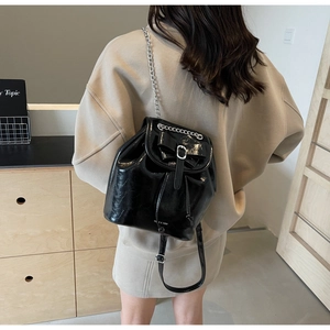 Detail of a black patent leather backpack with bow accent and metallic chain straps
