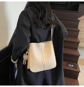 Macro detail of off-white lychee grain leather bucket bag with plush bear charm