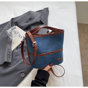 Detail of blue denim bucket bag with brown leather handles and adjustable shoulder strap