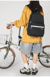 Detail view of a black canvas backpack for students with white zip pocket and brand tag