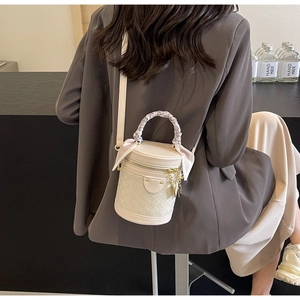 Detail of cream bucket bag featuring woven texture and silk scarf wrapped handle
