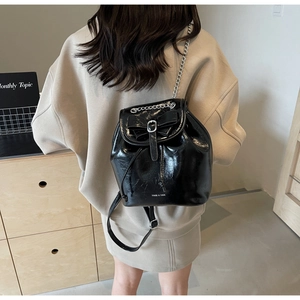 Detail of glossy black leather backpack featuring bow accent and silver chain straps