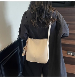 Detail of cream pebbled leather bucket bag with brown pom-pom charm on model back