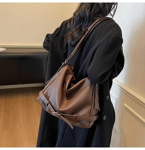 Detailed view of dark brown pebbled leather shoulder bag with buckle strap on a model