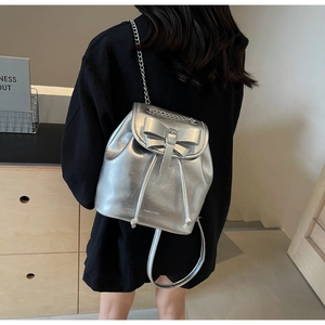 Detail of silver metallic backpack with bow accent, drawstring and chain strap on model