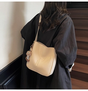 Beige litchi grain bucket bag with brown plush pendant worn on black coat