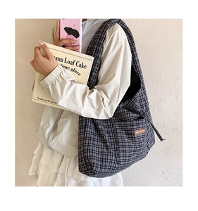 Detail of blue plaid canvas tote bag with side pocket and brown leather label accents