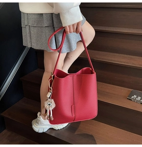 Close-up of red lychee pattern leather bucket bag with plush ball charm on wooden stairs