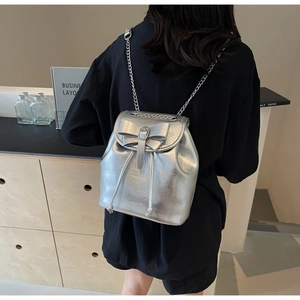 Detail of silver metallic backpack with bow decoration and chain strap on person