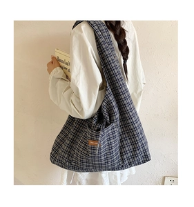 Detailed view of blue and grey plaid tote bag with brown leather brand tag on side