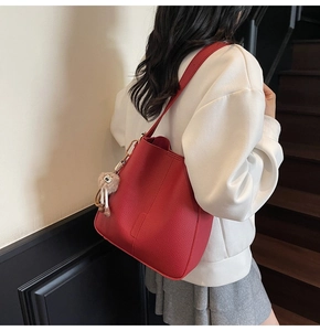 Detail of red pebbled leather tote bag featuring a cute plush bear charm on the strap