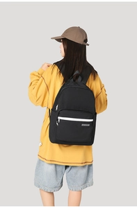Detailed back view of a minimalist black canvas backpack featuring white metal zippers