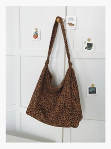 Détail du sac cabas léopard avec bandoulière à nœud décoratif sur fond de bois blanc