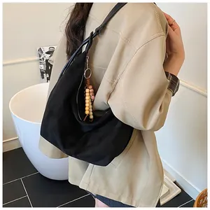 Black canvas hobo bag on shoulder featuring wooden bead charm and minimalist half-moon shape