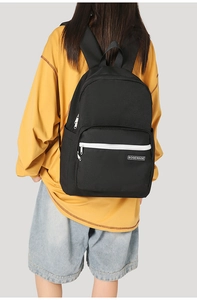 Detail of black canvas backpack with contrast white zipper and brand label on model