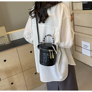 Detail of black woven bucket bag featuring gold zippers and a decorative silk scarf handle