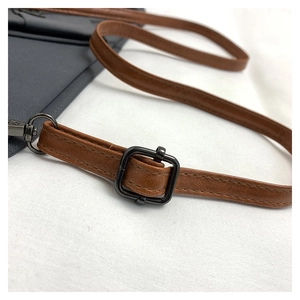 Detailed macro view of adjustable brown leather strap and dark metal buckle on gray bag
