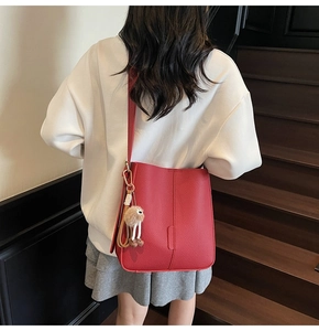 Detail of red lychee pattern bucket bag with a cute plush doll charm on a leather strap