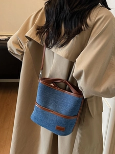 Blue denim bucket bag with brown leather trim shown on model wearing khaki trench coat