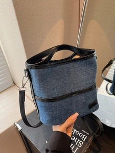 Retro denim bucket bag with black leather trim and a top handle shown in a lifestyle setting