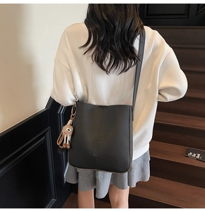 Detail of black pebbled leather bucket bag with cute plush lion charm worn by model
