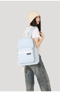 Close-up of light blue canvas backpack with black brand label and front zipper pocket