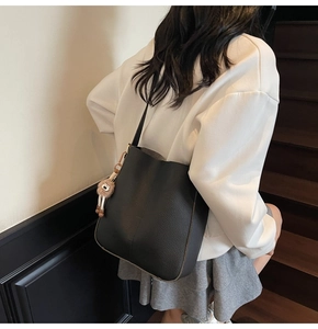 Detail of a black textured bucket bag with a plush charm on an indoor staircase