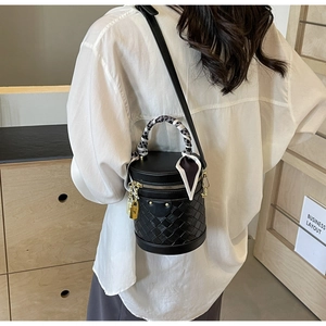Detail of black cylindrical bucket bag featuring woven base and silk scarf wrapped handle