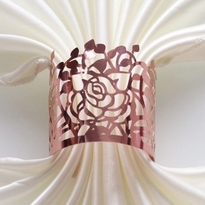 Close-up of laser-cut rose gold napkin ring with intricate floral pattern on white silk