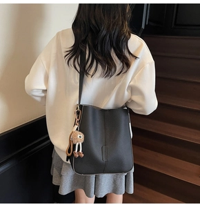 Close-up of black litchi pattern bucket bag with a cute brown plush pendant on stairs