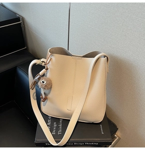 Detailed close-up of beige pebbled leather bucket bag with brown plush pom-pom charm