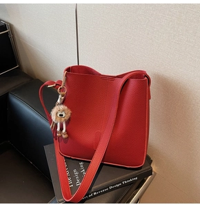 Detailed macro of red lychee pattern bucket bag with white plush eye pendant on leather chair