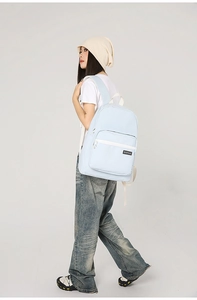 Side view of a light blue canvas backpack worn by a model for a casual street style look