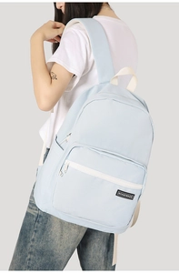 Light blue water-resistant nylon backpack with white zippers shown on model from side-rear view