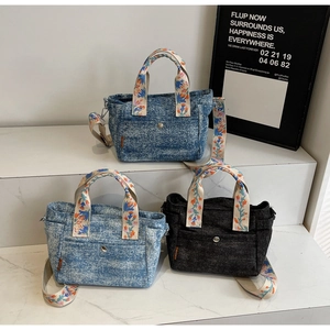 Detail of denim tote bags with floral embroidered straps in blue and black colors
