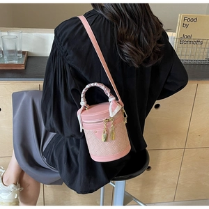 Pink bucket bag with woven texture, silk scarf handle, and gold hardware on a wooden table