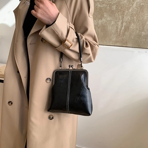 Detail of vintage black kiss-lock handbag with white stitching on beige coat background