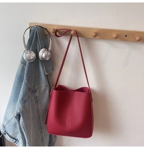Detail of red lychee grain leather bucket bag hanging with denim jacket and headphones